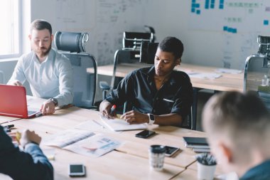Formal giyim iş projesi üzerinde brifing sırasında modern ofis toplantı masasında oturan işbirliği yaratıcı meslektaşlarının çok kültürlü takım giymiş. Profesyoneller oturum beyin fırtınası