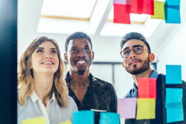 Çok kültürlü grubu renkli çıkartmalar Office cam duvar arkasında üzerinde yazılı notlar okuma creatie kadın ve erkek arkadaşları. Pozitif çalışanlar yapışkan kağıt kullanarak görev üzerinde işbirliği yapma