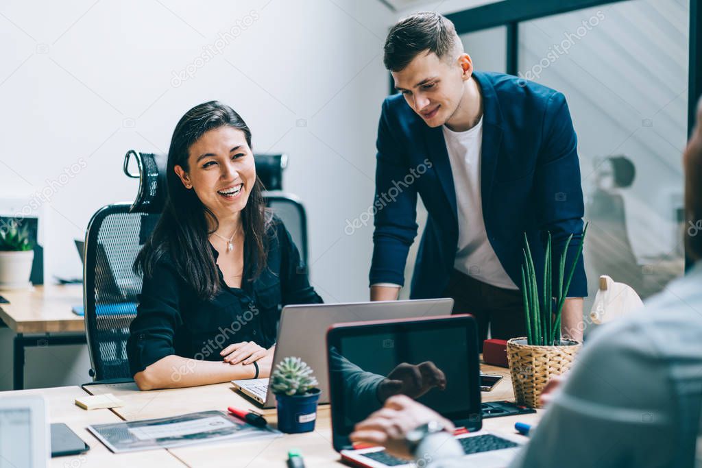 Multicultural positive male and female employees dressed in formal wear having fun during working process on project in modern office.Cheerful colleagues laughing while collaborating on task