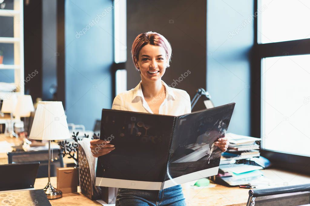 Half length portrait of female fashion designer holding sketchbook satisfied with completing creative task, happy businesswoman holding report of project planning smiling and looking at camer