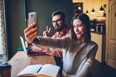 Pozitif genç öğrenciler komik selfies fotoğrafları smartphone ön kamera üzerinde görev çalışmaya işbirliği sırasında yapma. Neşeli genç kadın ve adam üstünde hareket eden telefon fotoğraf çekmek
