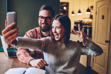 Mobil uygulama smartphone Yayın sosyal ağlar için yüklü komik selfies yapma rahat giyim mutlu duygusal hipster blogcular. Neşeli ve erkek öğrencilerin fotoğraf çekmek