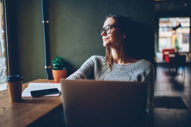Pencereden dışarı bakıyor ve yaratıcı fikirler üzerinde şık coworking alanda dinlenme dizüstü bilgisayar ile mesafesi iş modern netbook, Pondering öğrenci sırasında düşünme rüya gibi genç kadın serbest meslek