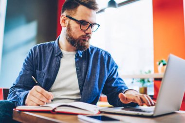 Genç işadamı çalışma takvimi veritabanı kullanarak bir not defteri içinde aşağı yazma modern dizüstü bilgisayarda kablosuz internet ile indirilebilir. Öğrenci ders için Web sitelerinde bilgi arama sakallı