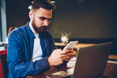 Sakallı blogger posta denetleme ve online sosyal ağlar üzerinden uzaktan alan coworking içinde modern dizüstü bilgisayarda çalışan süre 4 g internet bağlantısı smartphone aygıt üzerinde takipçileri ile sohbet