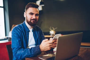 Yarım uzunluk portresi başarılı akıllı netbook kafede oturan ücretsiz Wi-Fi bağlantısı üzerinden arkadaşlarınızla çevrimiçi sohbet mesajlaşma blogger sakallı. Pozitif hipster adam yükleme uygulaması
