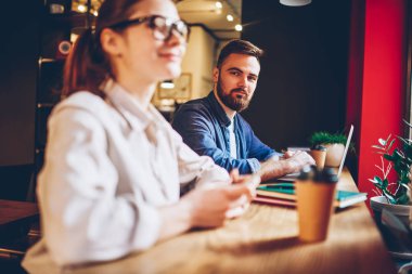 Sakallı genç adam ile öğrenci alan coworking içinde ortak tasarım proje üzerinde işbirliği yaparken kameraya bakan yarım uzunluk portre. İki tasarımcıları teamworking kafede oturan ev ödevi üzerinde