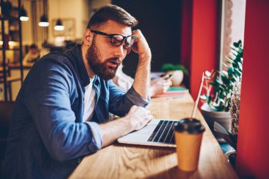 Yorgun sakallı öğrenci sınava hazırlık şık coworking uzayda sırasında modern dizüstü bilgisayar başında oturan uyuyor. Genç adam stresli bir gün sonra dijital netbook mesafe iş sırasında uyuklayan bitkin