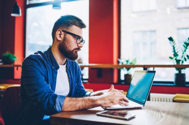 Dalgın sakallı erkek freelancer metin dijital netbook klavyede yazarak kablosuz internet'e bağlı. Hipster öğrenci ders için Web sitelerinde bilgi arama. Genç adam uzaktan çalışma
