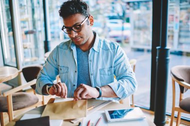 Kırpılmış görüntü ciddi iyi görünümlü akıllı erkek hindu işadamı gözlük göz koruma kağıt zarfın içinde koyarak için. Parsel kafede yakışıklı dalgın adam alarak mektup