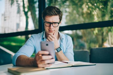 Gözlük sağlamak gözleri koruma ücretsiz 4 g internet bağlantısı kullanarak modern smartphone aygıtında haber okumak için şüpheci genç adam. Hipster adam hücresel cihaz üzerinde online video izliyor