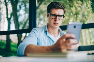 Ücretsiz 4 g internet bağlantısı kullanarak modern smartphone aygıt üzerinde gelen sorgulama bildirim okuma gözlük belirsiz genç adam. Şüpheli hipster adam cep blogda video izliyor