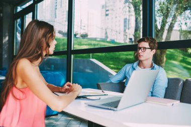 Dizüstü bilgisayar cihaz ile kablosuz internet bağlantısı oturan ve birbirleri ile modern kafede başlangıç projesi için yaratıcı fikirler hakkında iletişim yetenekli iki hipster öğrenciler