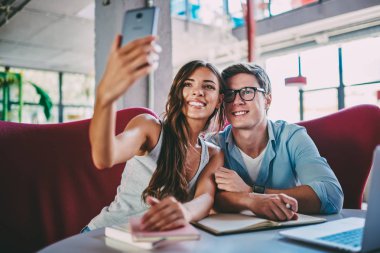 Gülüyor ve selfie alan coworking içinde sınava hazırlık sırasında modern smartphone yapma olumlu hipster öğrenci. Mutlu çift ön kamera telefon ve blog alarak fotoğraf gülümseyen aşık