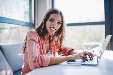 Modern dizüstü bilgisayar klavye üzerinde bilgi yazarken kameraya gülümseyen neşeli çekici genç bir kadın portresi. Pozitif kadın serbest meslek sahibi App dijital netbook üzerinde güncelleştirme