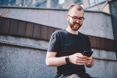 Neşeli sohbet online sosyal ağlar üzerinde modern smartphone ücretsiz 4 g kullanarak Eyewear genç adam sakallı Internet. Pozitif hipster blogger arkadaş dijital hücresel mesajlaşma süre gülüyor