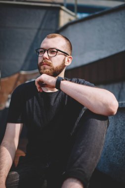 Optik gözlük vizyon düzeltme şehir kentsel ortamda oturan düşünceli boncuklu genç adam. Boş zamanlarında Caddesi üzerinde dinlenme ve yaratıcı fikirler üzerinde düşünme Eyewear durulması hipster adam