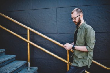 Hücresel üst katta devam app yükleme Hipster adam rahat kıyafet profil sayfası modern smartphone açık havada, yürüyüş 4 g internet bağlantısı kullanarak güncelleştirme dalgın genç adam blogger giymiş