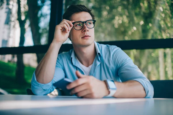 体贴的年轻男子博客在时尚眼镜视力矫正的视线和思考的创意 在手和坐在 Coworking 空间的智能手机出版物 — 图库照片