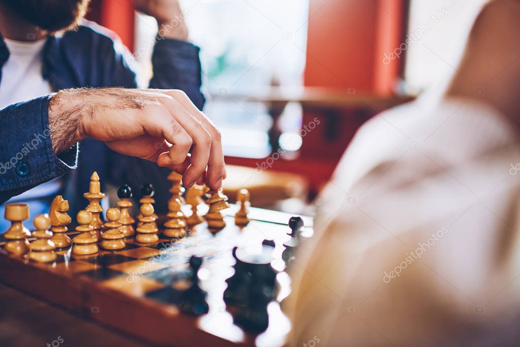Cropped image of male hands making move of white pawn on wooden chessboard during strategic game in chess sitting in coworking.Selective focus on sport battle in tactic play with chess