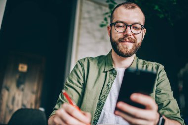 Aşağıda pozitif görünümü kullanarak 4 g Smartphone cep telefonu ile takipçileri komik bildirim okunurken gülen genç adam sakallı Internet. Video izlerken gülmekten gözlük neşeli hipster adam