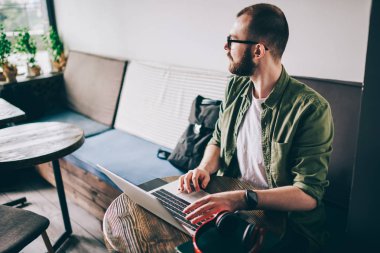 Düşünceli genç modern bilgisayarda kablosuz internet kafede oturan kullanarak yükleme uygulama adam. Uzak mesafe işi sırasında yazılım netbook üzerinde güncelleştirilirken seyir durulması hipster adam