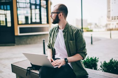 Düşünceli genç adam deniz dizüstü cihazda klavye Eyewear? ch bilgi web sitesi ve uzak oturma açık havada içinde kentsel ayarı arıyorum. Netbook uzaktan çalışma durulması hipster adam