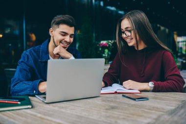İşbirliği olumlu ve erkek öğrenciler e öğrenme, kafe Teras, teen hipsters projeden gelen bilgileri ararken birbirinizle konuşmak gülümseyen oturmak için dizüstü bilgisayar kullanan