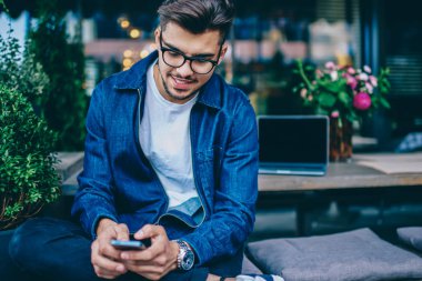 Sosyal ağlar üzerinde boş zaman, yakışıklı hipster adam cep telefonu kablosuz internet kafede sohbet için bağlanma smartphone kullanarak bildirim kontrol Gözlük Genç beyaz erkek