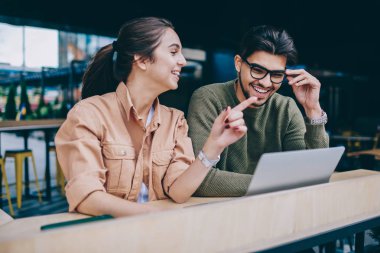 Neşeli ve erkek öğrencilerin ödev birlikte, gülümseyen hippi kız erkek komik şakalara gülüyor konuşurken bir şey üzerinde işaret yapmayı işbirliği olumlu konuşmayı