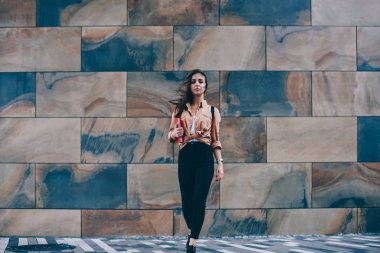 Modaya uygun kıyafet ayakta duvara tanıtım alanı reklam metin mesajları, kamera açık havada seyir casual giyim giymiş genç kadın için çekici hippi kız portresi tam uzunlukta