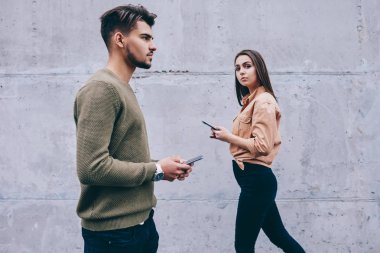 Genç kadın ve akıllı telefonlar ile açık havada yürüyen adam gerçek iletişim prefere online, hipsters bağımlılığı duvar arka plan üzerinde geziniyor modern teknolojilere sahip smartphone kullanarak sohbet yoksay