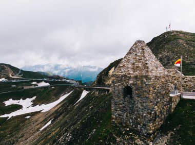 Bulutlu gökyüzünün altındaki karlı dağlarda kuş bakışı yol manzarası. Avusturya 'da Grossglockner High Alpine Road adlı manzaralı bir rota. Hochtor Geçidi 'nin bir kısmı.
