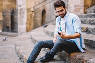 Hipster adam okuma bildirim şehirdeki merdivenlerde dinlenme Smartphone cep telefonu ile gülümseyen, sakallı erkek blogger paylaşmak fotoğraf--dan gezi ve sosyal ağlar üzerinde hücresel açık havada takipçileri ile sohbet