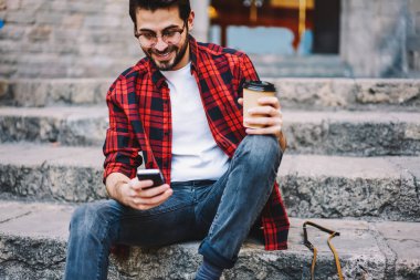 Hipster adam cep şehirde iyi 4 g bağlantısı üzerinden video izlerken gülümsüyor, smartphone uygulama kahve ile dinlenme gitmek için sosyal ağlarda profil kontrol neşeli erkek blogger güncelleştirmeleri
