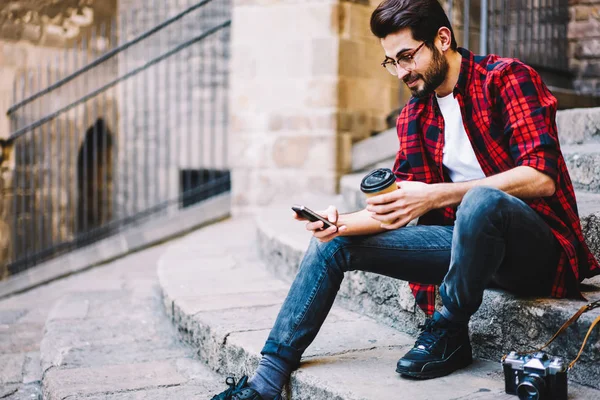 Young man in casual wear checking mail on smartphone usign 4G connection on street,hipster guy confirming new friend in social networks share pictures and multimedia with followers sitting outdoors