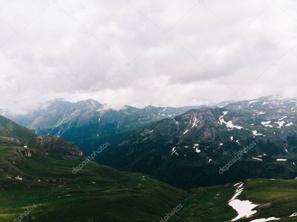 Beautiful scenery view of mountains peaks on hight altitude covered with grass and intervals of snow.  Foggy and cloudy weather