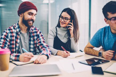 Pozitif meslektaşları office projesinde birlikte çalışma sırasında gülüyor rahat kıyafet giymiş. Smartphone üzerinde arama ve notlar yaparken gülümseyen erkek çalışan ile işbirliği başarılı genç kadın
