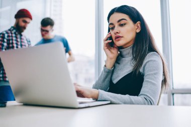 Dizüstü bilgisayarda kablosuz internet kullanarak e-posta kontrol ederken smartphone üzerinde arama ciddi iş kadını. Dalgın öğrenci netbook masaüstü ofis oturma, çalışma sırasında telefonla konuşuyor