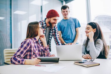 Başarılı grup genç profesyonellerin rahat kıyafet laptop ofiste oturan tasarım proje üzerinde işbirliği sırasında gülüyor. Beyin fırtınası sırasında ortak görev üzerinde olumlu öğrenciler teamworking