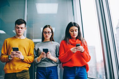 Duvara yakın duran ve akıllı telefonlar üzerinde online sohbet mesajlaşma dalgın hipster blogcular. Canlı iletişim görmezden sosyal ağlardan bağımlısı rahat kıyafet bin yıllık gençlerin antisosyal