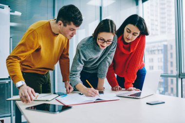 Takım içinde çalışma ve çizim dalgın hipster öğrenciler ayakta üzerinden masaüstü ofis içinde laptop ile kroki. Genç kadın beyin fırtınası toplantısı meslektaşları ile iş projesi için notları yazma