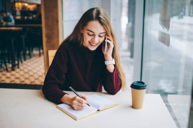 Mutlu neşeli kadın blogger Üniversitesi kafeterya, teknoloji ve iletişim kavramı, mobil uygulaması aracılığıyla arkadaşıyla konuşurken ders kitabı kendi içerik Web sitesi için yeni makale oluşturma