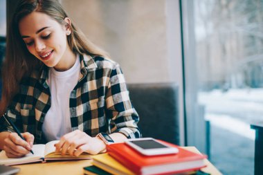 Sosyal ağlar, yeni takipçileri çekmek için kendi içerik Web sitesi pencere yakınındaki Üniversitesi Kütüphanesi'nde otururken mutlu kadın planlama gezi için yeni makale yazıyorsun, pozitif kadın blogger