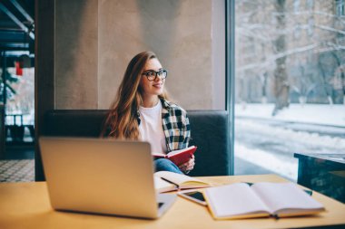 Pozitif gülümseyen hippi kız giyim gözlük vizyon düzeltme bilgisayarı kullanmak ve sınav için hazırlanıyor süre uzağa arıyorsunuz ve bekleyen arkadaş kitap okuma coworking uzay zaman geçirmek için