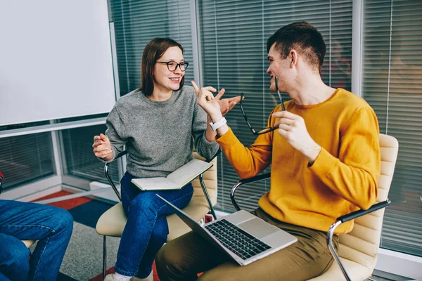 Positive hipster students dressed in casual wear arguing with each other having brainstorming meeting in classroom during courses.Cheerful young man and woman emotionally discussing working project