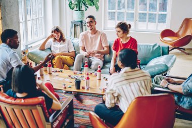 Modern daire poker masasında oynarken gülüyor olumlu çeşitli hipsters oyun. Neşeli çok kültürlü rahat giyinmiş genç erkek ve kadınların eğleniyor düz eğlence zevk
