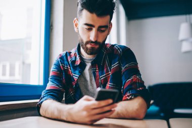 Kampüs, bin yıllık erkek cep telefonuyla haber sosyal ağlar üzerinden kablosuz internet kapalı okumak içinde otururken Smartphone'da app üzerinden para işlem yapma ciddi genç hipster adam