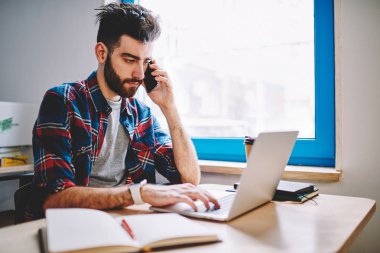 Genç ciddi grafik tasarımcı dizüstü bilgisayar, netbook bilgi arama wifi bağlı konsantre adam yeni logo oluşturulurken önemli cep telefonu üzerinden muhabbet