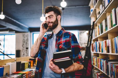 Başarılı adam olumlu hücresel yeni uygulama ile Üniversitesi kampüsünde muhabbet gülümseyen, mutlu hipster adam giymek Kitabevi, serbest zaman zevk ve teknolojisini kullanarak rahat konum